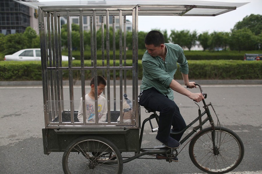 Tiểu Hào là một cậu bé năm nay 10 tuổi, ở Thái Châu, Chiết Giang, Trung Quốc. Không giống như bạn bè cùng trang lứa, Tiểu Hào không thể tự chăm sóc mình bởi căn bệnh bại não quái ác. Trong ảnh: Cha Tiểu Hào  nhốt con trong cũi đưa đi chơi.