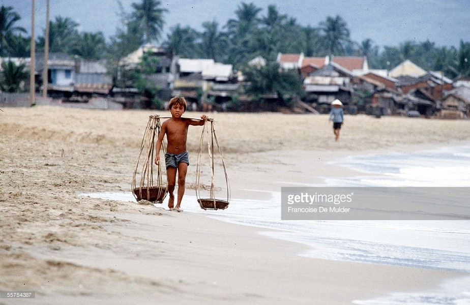 Một cậu bé quẩy đòn gánh trên bãi biển Nha Trang. Hình ảnh nằm trong loạt ảnh  Việt Nam năm 1985 của nữ phóng viên ảnh người Pháp nổi tiếng Francoise De Mulder.