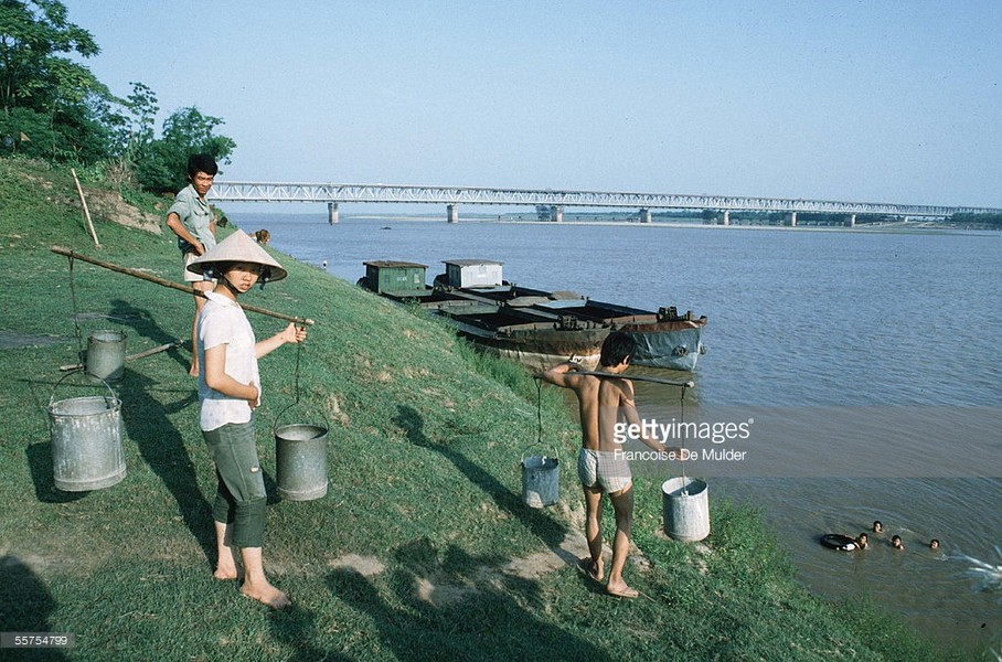 Người dân gánh nước tại bãi sông Hồng gần cầu Chương Dương. Hình ảnh nằm trong loạt ảnh  Việt Nam năm 1985 của nữ phóng viên ảnh người Pháp nổi tiếng Francoise De Mulder.