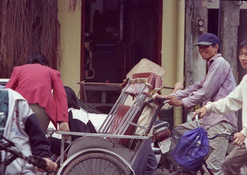 Nụ cười của người lái  xích lô trên phố Bà Triệu giờ cao điểm buổi sáng, Hà Nội năm 1995. Lúc này hai người khách đang xuống xe. Ảnh: Yuichi Kobayashi Facebook.