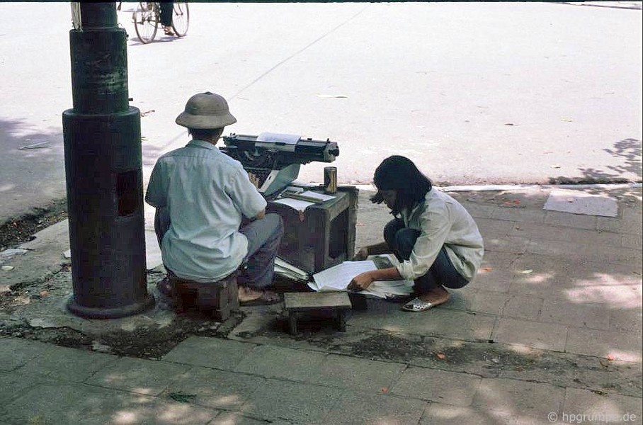 Một người đàn ông ngồi đánh máy chữ ở một ngã tư của khu phố cổ Hà Nội năm 1991. Nghề đánh máy chữ ở  Hà Nội đầu thập niên 1990 đã biến mất cùng sự hiện diện của các cửa hàng photocopy, in vi tính. Ảnh: Hans-Peter Grumpe/Hpgrumpe.de.