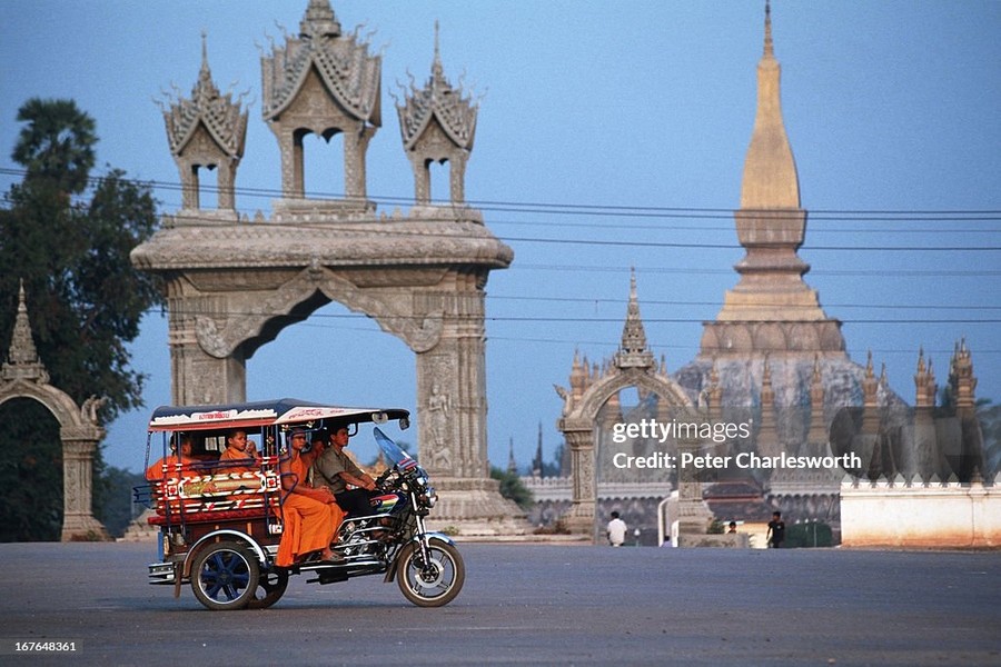 Chiếc xe tuk tuk chở các nhà sư đi ngang qua Pha That Luang, ngôi chùa lớn và nổi tiếng nhất thủ đô Vientiane,  Lào năm 1991. Ảnh: Peter Charlesworth / LightRocket via Getty Images.