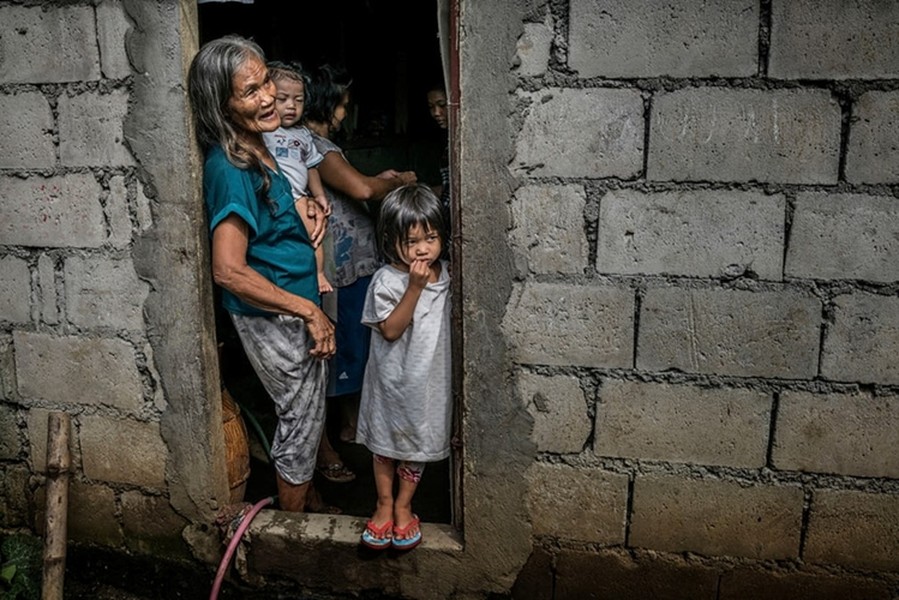 Remy Fernandez, 84 tuổi, bế đứa cháu nội của bà tại nhà ở Patayas, Manila. Fernandez hiện là người nuôi dưỡng 7 đứa cháu sau khi con trai bà, Constantino de Juan, bị giết trong  cuộc chiến chống ma túy ở Philippines. Mẹ của những đứa nhỏ hiện chịu án tù giam do buôn bán ma túy. Ảnh: Guardian.