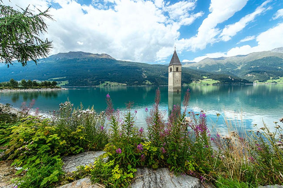  Hồ Reschen, Bolzano - Ý: Reschensee hoặc hồ Reschen là một hồ nhân tạo ở phần phía tây của Nam Tyrol, Ý, khoảng 2 km về phía nam của đèo Reschen, tạo thành biên giới với Áo, và 3 km về phía đông của sườn núi tạo thành biên giới với Thụy Sĩ. Hồ nổi tiếng với gác chuông của một nhà thờ thế kỷ 14 bị ngập nước, khi mặt nước đóng băng có thể đi bộ trên đó. Một truyền thuyết nói rằng trong mùa đông người ta vẫn có thể nghe thấy tiếng chuông của nhà thờ. Nhưng thực tế, những chiếc chuông được lấy ra khỏi tòa tháp vào ngày 18 /7/ 1950, một tuần trước khi phá hủy nhà thờ và tạo ra hồ.