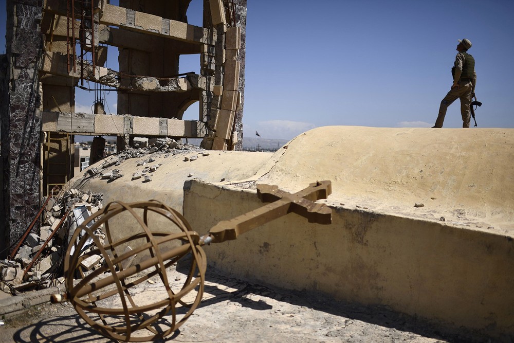 Một dân quân đứng gác trên nóc nhà thờ Thánh John ở  thị trấn Qaraqosh, cách thành phố Mosul khoảng 30 km, ngày 16/4/2017. Một số gia đình đã quay trở về thị trấn này sau thời gian “chạy loạn”. Ảnh: The Atlantic.