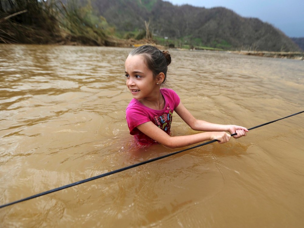 Siêu bão Maria mạnh cấp 4 đã tàn phá Puerto Rico vào ngày 20/9 và gây ra cuộc  khủng hoảng nhân đạo tại hòn đảo này. Do ảnh hưởng của bão, cho đến nay phần lớn Puerto Rico bị mất điện. Ngoài ra, thực phẩm, nước uống và nhiều mặt hàng cần thiết khác đều khan hiếm. Ảnh: Bé Ruby Rodriguez (8 tuổi) lội qua sông ở Morovis. Ảnh: BI.