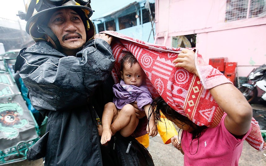 Nhân viên cứu hộ giúp đỡ một phụ nữ và con nhỏ sơ tán khỏi một khu ổ chuột ở Manila.