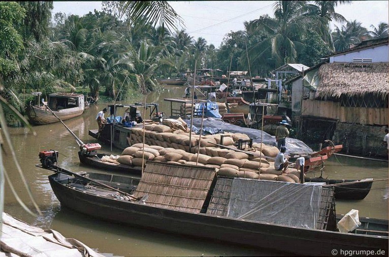 Những con thuyền chất đầy những bao tải gạo bên một bến sông. Ảnh: Hans-Peter Grumpe.