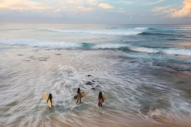 Tại bãi biển Makaha ở Oahu, Hawaii, hai chị em ruột cùng một người em họ chạy trên những con sóng để làm nóng người trước khi tham gia cuộc thi lướt sóng. Tham gia môn thể thao truyền thống này từ nhỏ sẽ giúp trẻ em ở đây tự hào về nền văn hóa của vùng đất mình sống. Ảnh:  NatGeo.