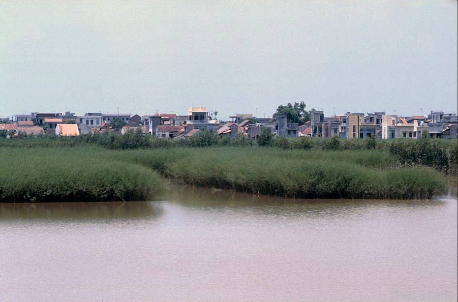  Làng gốm Bát Tràng nhìn từ sông Hồng, 1991. Đây là một làng gốm cổ nằm ở huyện Gia Lâm, ngoại thành Hà Nội. Tên gọi Bát Tràng được hình thành từ thời Lê, đó là sự hội nhập giữa 5 dòng họ gốm nổi tiếng của làng Bồ Bát xứ Thanh với dòng họ Nguyễn ở đất Minh Tràng.