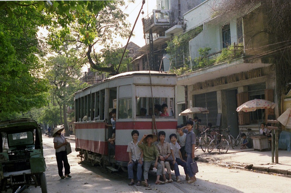 Đám trẻ em ngồi sau toa  tàu điện trên phố Quán Thánh, trước hiệu sách nhân dân Ba Đình (ngày nay là hiệu sách Ba Đình, 12 Quán Thánh), Hà Nội năm 1990. Ảnh: Ian Lynas Flickr.