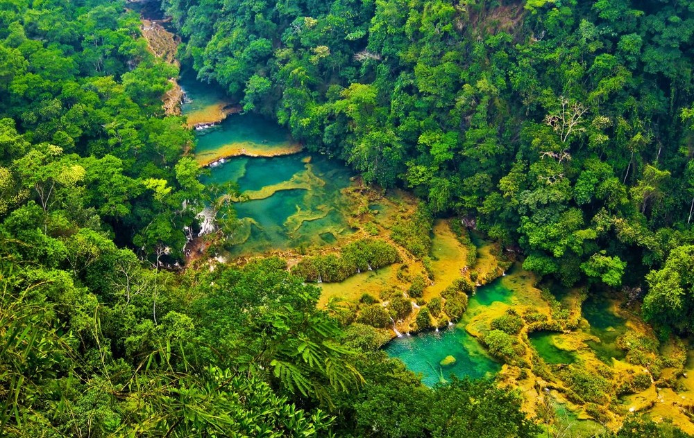  1. Semuc Champey. Semuc Champey là một loạt các cây cầu tự nhiên và hang động đá vôi nằm ở miền trung  Guatemala. Điểm đến biệt lập này là nơi du khách đắm mình trong làn nước trong vắt, mát lạnh của những hồ bơi tự nhiên tuyệt đẹp, giữa khung cảnh núi rừng hùng vĩ, hoang sơ.