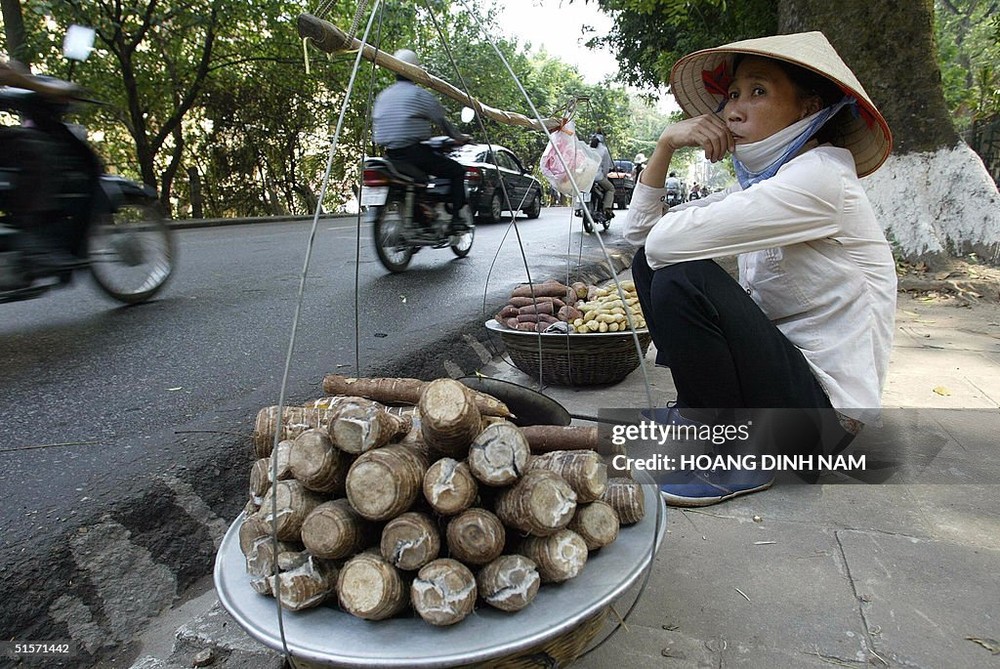 Một người phụ nữ ngồi bán khoai lang và sắn luộc trên đường Hoàng Hoa Thám,  Hà Nội ngày 26/10/2004. Ảnh: Hoang Dinh Nam / AFP via Getty Images.