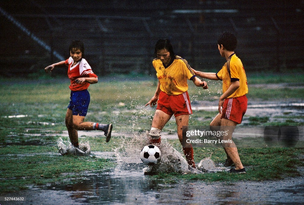 Ba nữ cầu thủ trẻ đá bóng trong cơn mưa lớn ở thị xã  Cẩm Phả năm 1997. Gia đình họ làm việc tại các mỏ than ở địa phương. Ảnh: In Pictures Ltd./Corbis via Getty Images.