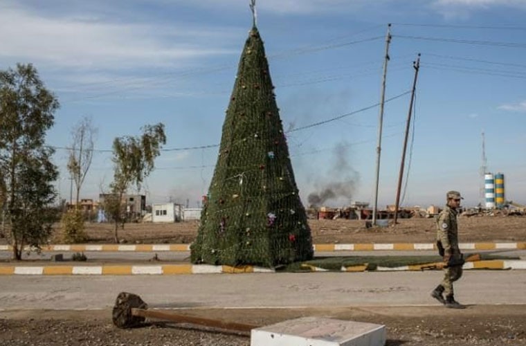 Hòa chung không khí  Giáng sinh trên khắp cả nước, những người dân Iraq theo đạo Thiên chúa cũng háo hức chuẩn bị đón ngày lễ quan trọng này. Ảnh: Một chiến binh theo đạo Thiên chúa đi ngang qua cây thông Noel dựng ở giữa con đường ở thành phố Mosul, nơi mới được giải phóng khỏi phiến quân IS. Ảnh Telegraph