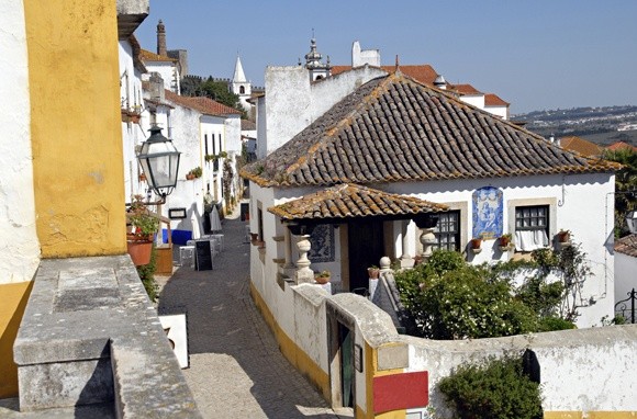 Làng Obidos thuộc tỉnh Estremadura (Bồ Đào Nha) là một trong những điểm đến thu hút du khách năm châu.  Ngôi làng bí ẩn ở Châu Âu này đẹp mỹ miều nằm trên đỉnh đồi và được bao quanh bằng tường thành kiên cố. Những bức tường, con đường, quảng trường và thành trì đồ sộ là điểm nhấn của ngôi làng đẹp như tranh vẽ này. Đến đây, bạn sẽ có cơ hội ngắm nhìn vẻ đẹp trường tồn của lâu đài thời trung cổ Obidos, Nhà thờ Xứ đạo Santa Maria, quán cà phê san sát và những ngôi nhà màu trắng được tô điểm bằng chậu hoa rực rỡ.