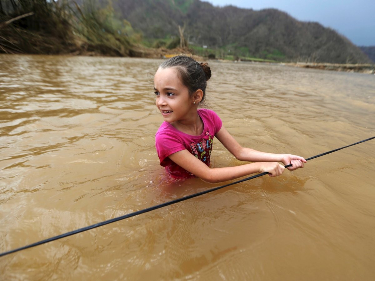 Siêu bão Maria mạnh cấp 4 đã tàn phá Puerto Rico vào ngày 20/9 và gây ra cuộc  khủng hoảng nhân đạo tại hòn đảo này. Do ảnh hưởng của bão, cho đến nay phần lớn Puerto Rico bị mất điện. Ngoài ra, thực phẩm, nước uống và nhiều mặt hàng cần thiết khác đều khan hiếm. Ảnh: Bé Ruby Rodriguez (8 tuổi) lội qua sông ở Morovis. Ảnh: BI.