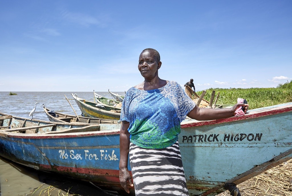 Bên bờ hồ Victoria ở phía Kenya, cô Justine Adhiambo Obura đang chăm chú nhìn vào một chiếc thuyền. Đó là buổi sáng bận rộn bên bờ hồ. Thuyền cập vào bờ mang đầy cá: cá rô sông Nile, cá da trơn, cá omena - hay còn gọi là cá mòi hồ Victoria. "Đó là chiếc thuyền đầu tiên của chiến dịch No Sex For Fish (Không  lấy tình đổi cá)", cô nói. Trong ảnh là Justine Adhiambo Obura, chủ tịch của hợp tác xã No Sex For Fish ở bãi biển Nduru, Kenya, đứng bên chiếc thuyền đánh cá của cô. Ảnh: NPR.