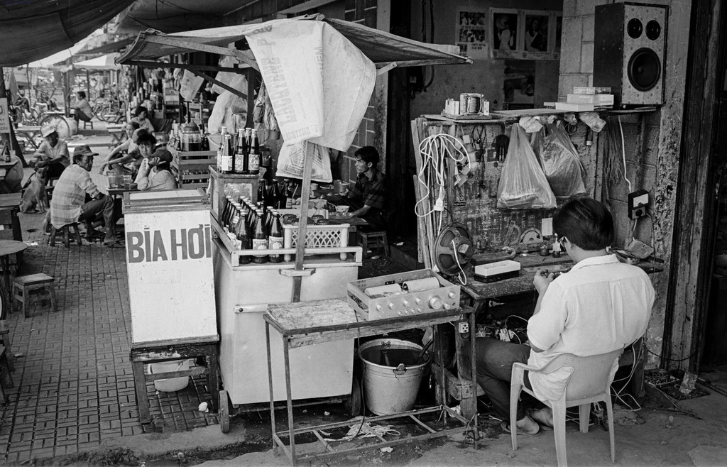 Một góc phố Sài Gòn với hàng sửa chữa đồ điện và quán giải khát, 1994. Hình ảnh nằm trong loạt ảnh  Sài Gòn thập niên 1990 do nhiếp ảnh gia người Mỹ Mike Huddleston đăng tải trên trang web Huddlestongallery.com