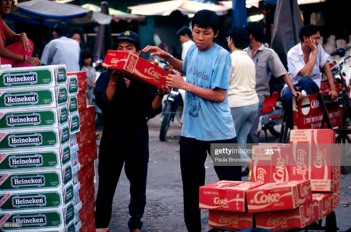 Hai nam giới bốc dỡ các thùng bia Heineken và nước ngọt Coca-Cola tại một khu chợ ở TP HCM, tháng 6/1993. Tại  Việt Nam năm 1993, các sản phẩm tiêu dùng phương Tây đã trở nên phổ biến. Ảnh: Paula Bronstein/Getty Images.