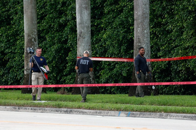 Bags hang from a fence over a rifle propped against it at Trump International Golf Club West Palm Beach