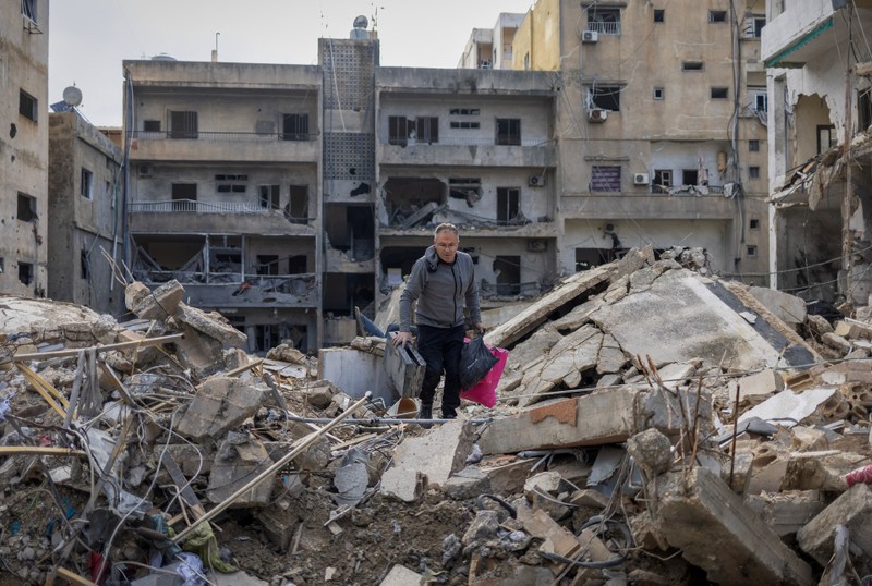 Samir Kassab, 53, carries his belongings as he walks on the rubble of his house destroyed in an Israeli strike in Tyre